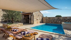Un espace piscine avec des chaises longues, une table sur laquelle se trouve une assiette de nourriture et une boisson, et un bâtiment en pierre avec un toit en tuiles.