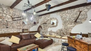 Un salon rustique avec des murs en pierre apparents, un canapé en cuir marron, une table basse en bois et un coin bar avec des tabourets.