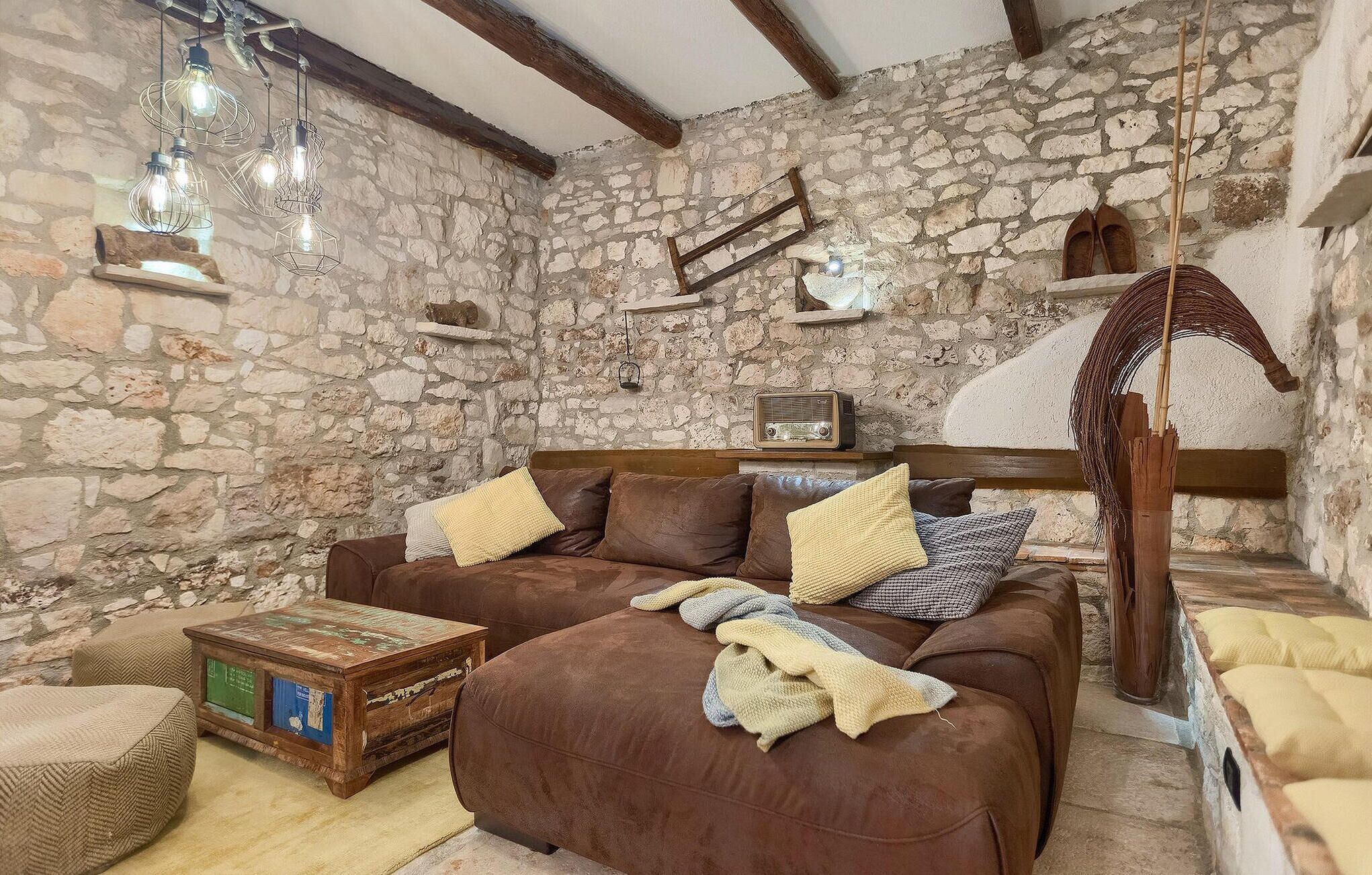 A rustic room with a stone wall, a wooden beam ceiling, a brown leather sofa, and a vintage radio.