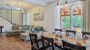 Ein gemütliches Wohnzimmer mit einer Couch, einem Hocker und einem Esstisch, der für das Frühstück gedeckt ist. Eine Treppe mit dekorativer Geländer führt zu einer weiteren Ebene.