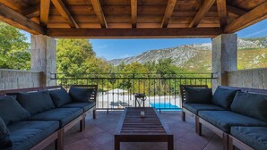 Ein überdachter Außenbereich mit zwei Sofas und einem Tisch, mit Blick auf einen Pool und Berge.