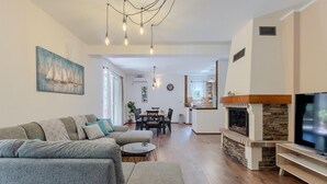 Ein modernes Wohnzimmer mit Sofa, Fernseher, Kamin, Essbereich und einer Küche im Hintergrund.