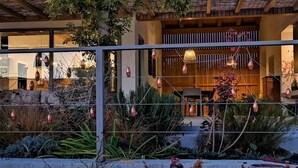 Un edificio moderno con fachada de vidrio, terraza de madera y luces decorativas colgantes.