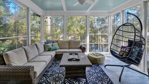 A sunroom with a large window, a ceiling fan, a sofa, a coffee table, and a hanging chair. - Hilton Lake Getaway w/ Hot Tub & Two Fire Pits (Chapin)