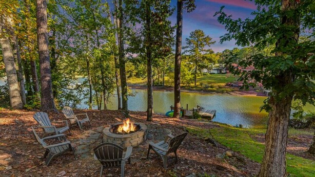 A fire pit surrounded by Adirondack chairs in a wooded area with a lake view. - Hilton Lake Getaway w/ Hot Tub & Two Fire Pits (Chapin)