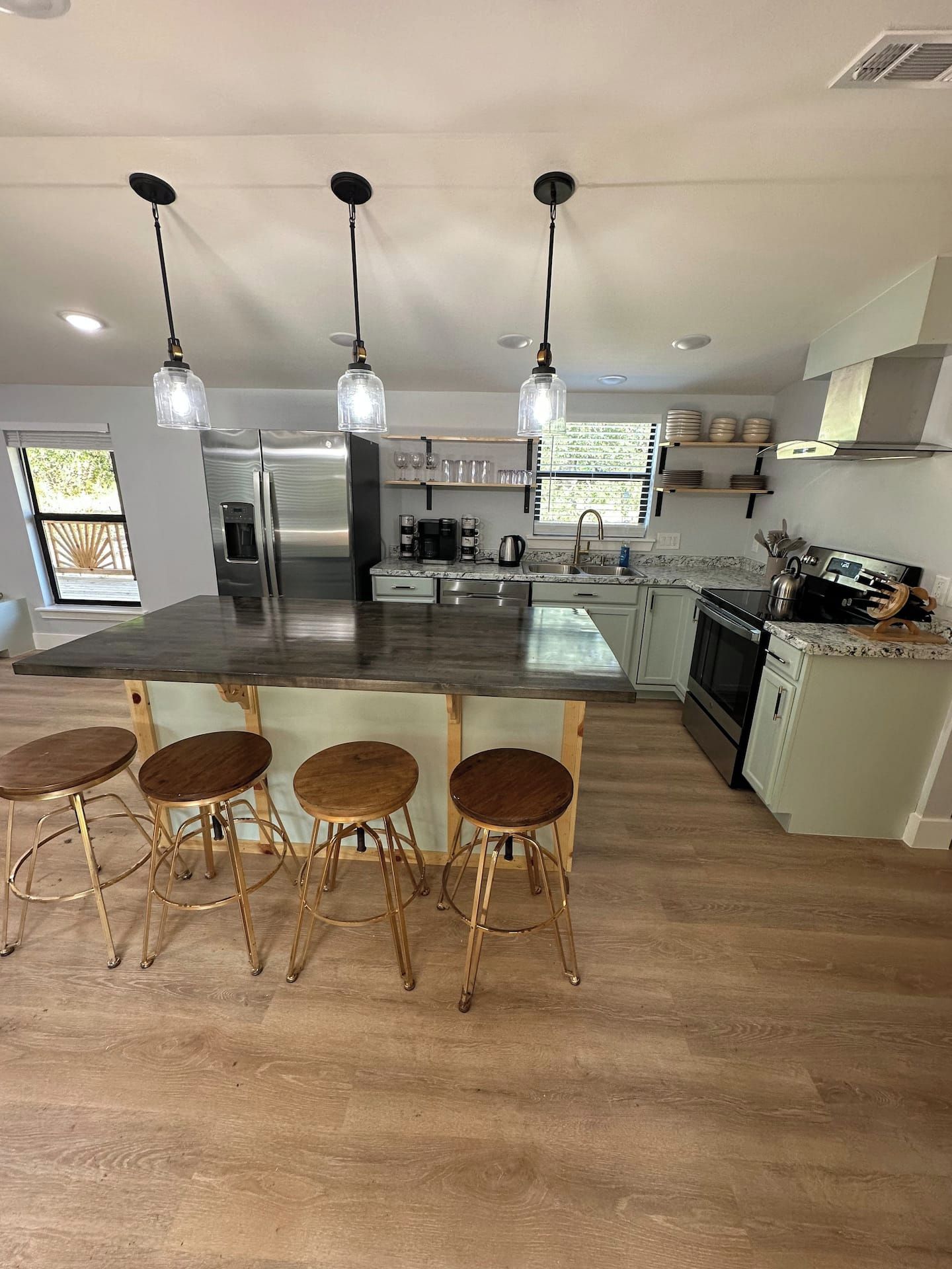 A modern kitchen with a central island, bar stools, stainless steel appliances, and pendant lighting.