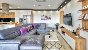 A modern living room with a grey sectional sofa, a coffee table, a flat-screen TV, and a wooden entertainment unit.