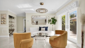 Een moderne woonkamer met een witte bank, twee fauteuils, een glazen salontafel en een grote spiegel.