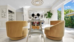 Een moderne woonkamer met twee comfortabele fauteuils, een Mickey Mouse stoel en een groot raam met uitzicht op groen.