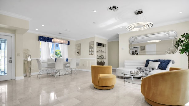 Een ruime woonkamer met een witte bank, twee gele fauteuils, een salontafel, en een eethoek met een witte tafel en stoelen.