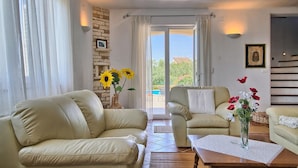 A living room with two beige leather sofas, a wooden coffee table, and a vase with flowers. There is a stone wall and a picture frame on the wall. - Gorgeous home in Pula (Pula)