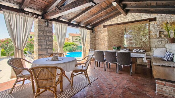 An outdoor patio with a round table and wicker chairs, a stone wall, and a view of a swimming pool. - Gorgeous home in Pula (Pula)