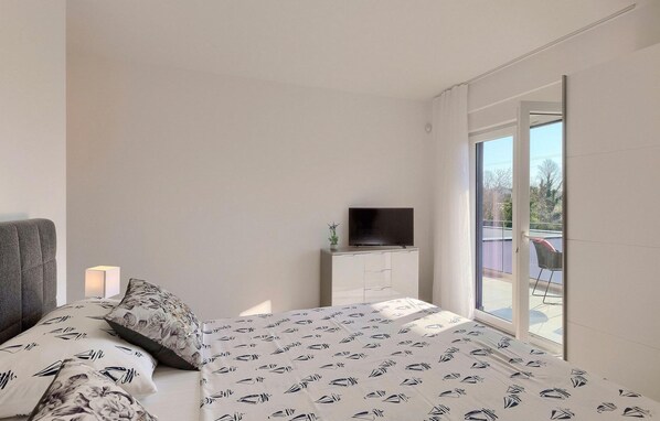 A bedroom with a bed, a bedside table with a TV, a window, and a view of the outside. - Lovely home in Liznjan (Liznjan)