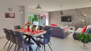 A modern dining area with a table set for six, surrounded by chairs. There is a sofa and a TV mounted on the wall in the living area. - Lovely home in Liznjan (Liznjan)