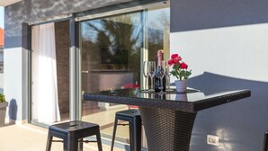 A modern outdoor bar area with a glass table, two bar stools, a bottle of champagne, and a potted plant. - Lovely home in Liznjan (Liznjan)