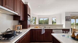 A modern kitchen with dark wood cabinets, a gas stove, and a large window providing a view of greenery outside. - Whale Watch Family & Pet Friendly Augusta Retreat (Augusta)