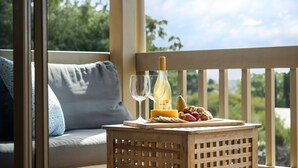 A wooden table with a bottle of wine, glasses, cheese, grapes, and pastries on a balcony with a view of greenery. - Whale Watch Family & Pet Friendly Augusta Retreat (Augusta)
