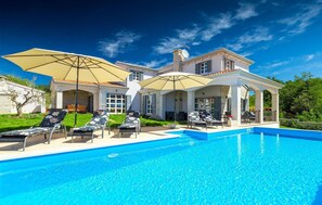 Una amplia casa con piscina, mobiliario exterior y un patio cubierto.