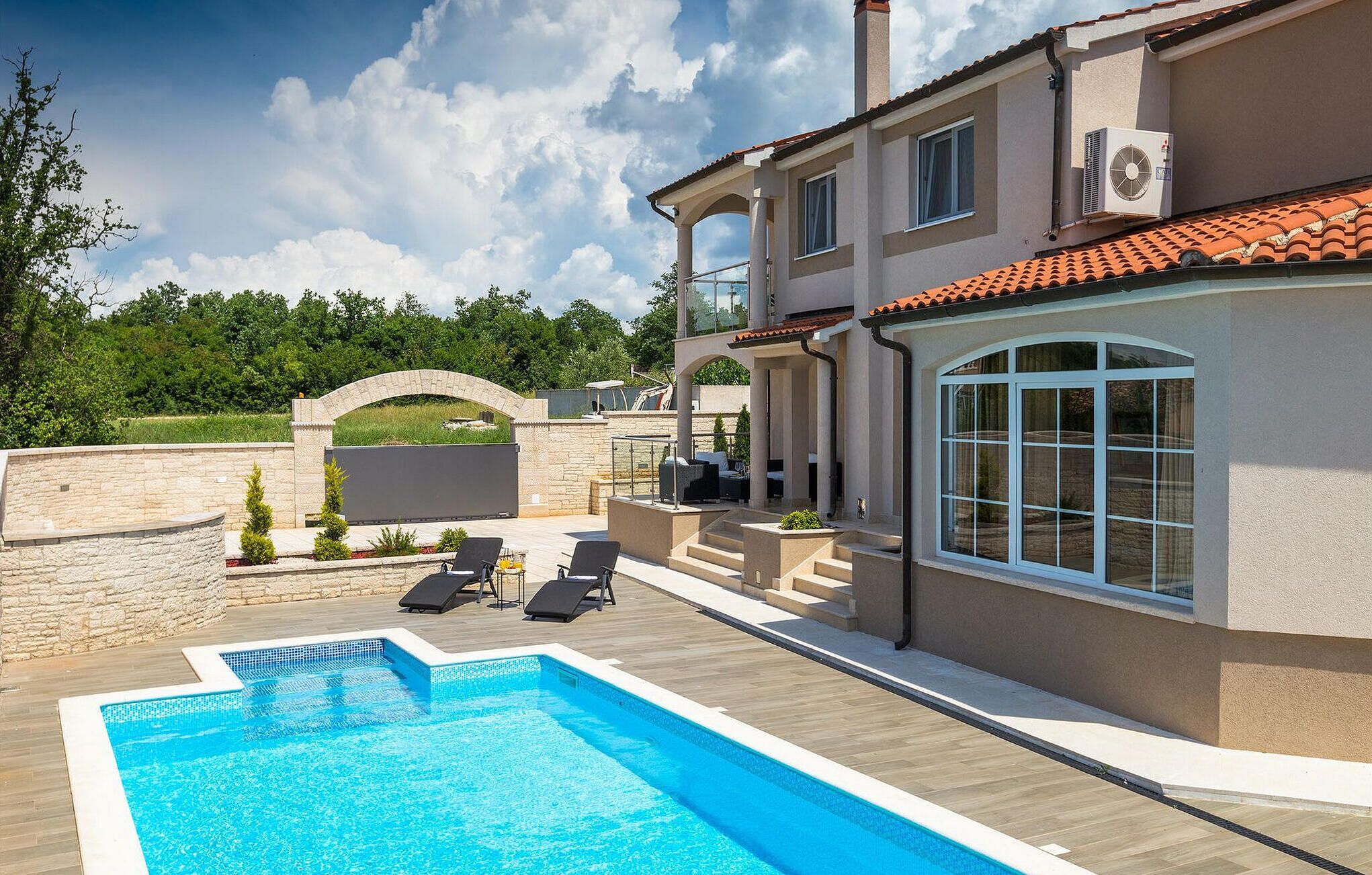 A modern villa with a swimming pool, outdoor seating, and a stone wall.