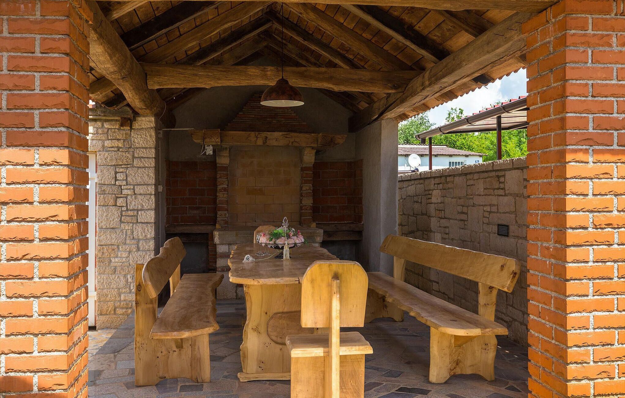 Ein Holz-Essbereich im Freien mit Bänken und einem Tisch, umgeben von Ziegelmauern und einem Steinboden.