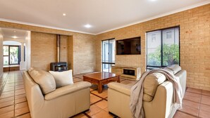 A living room with a fireplace, leather sofas, a coffee table, and a TV mounted on the brick wall. - Waterfront Bliss: Serenity & Adventure Await! (Geographe)