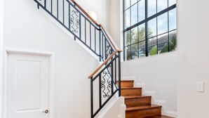 A staircase with a wooden handrail and black metal balusters, leading to a white door. - Waterfront Bliss: Serenity & Adventure Await! (Geographe)