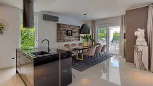 A modern kitchen with a glass island, a dining area with a table and chairs, and a view of the outdoors. - Stunning home in Umag (Umag)