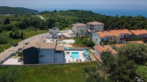 Un quartier résidentiel situé sur la côte, avec des maisons à étages, une piscine et une route qui serpente à travers le paysage.