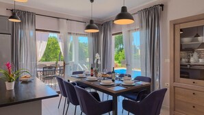 Uma sala de jantar moderna com uma mesa grande, cadeiras escuras e iluminação pendente.