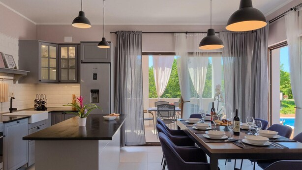Uma cozinha moderna com uma ilha central, uma área de jantar com mesa posta para quatro pessoas e vista para uma piscina.
