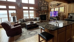 A spacious cabin interior with a stone fireplace, wooden ceiling, and large windows overlooking a lake. - Cozy Cabin on Lake Wisconsin
Skiing, Fishing & Hiking Retreat (Merrimac)