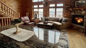 A spacious cabin interior with a stone fireplace, a large window overlooking a lake, a leather sofa, and a marble coffee table. - Cozy Cabin on Lake Wisconsin
Skiing, Fishing & Hiking Retreat (Merrimac)