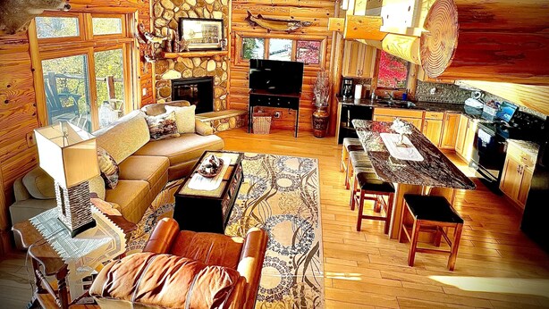 A log cabin interior with a stone fireplace, wooden furniture, and large windows. - Cozy Cabin on Lake Wisconsin
Skiing, Fishing & Hiking Retreat (Merrimac)