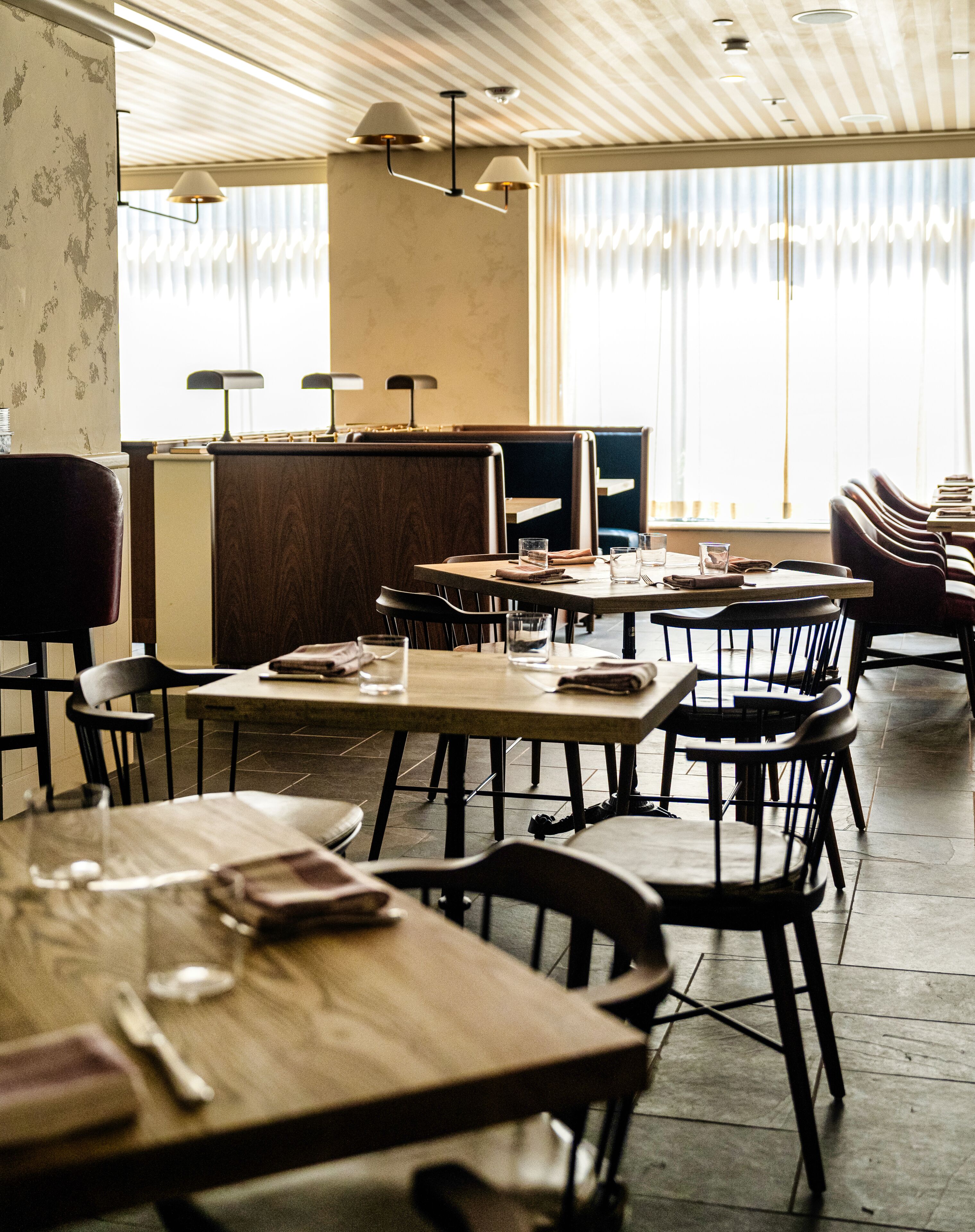 Een restaurant met houten tafels en stoelen, een toonbank en hanglampen.