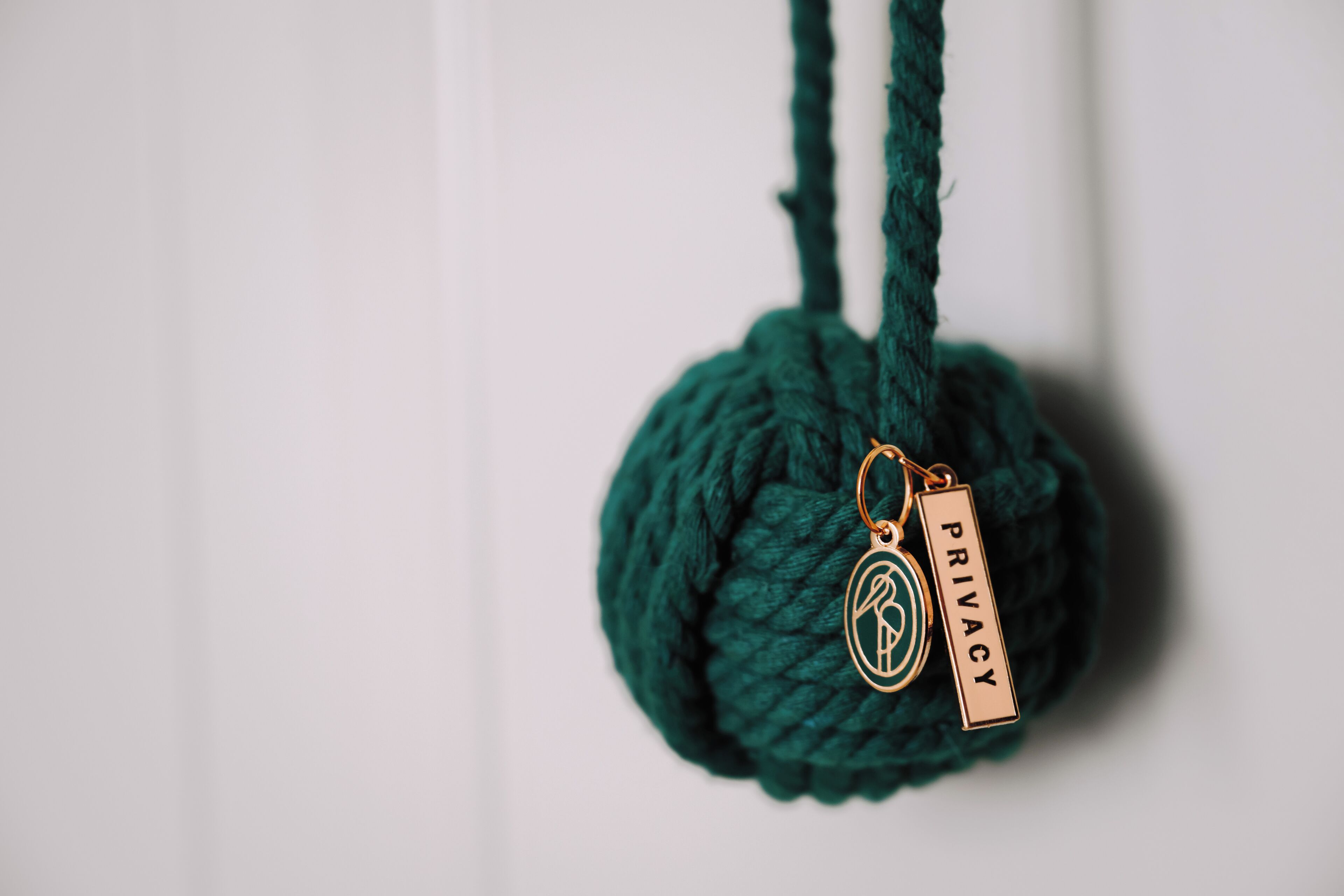 A green knitted ball with a metal tag labeled "PRIVACY" hanging from it.