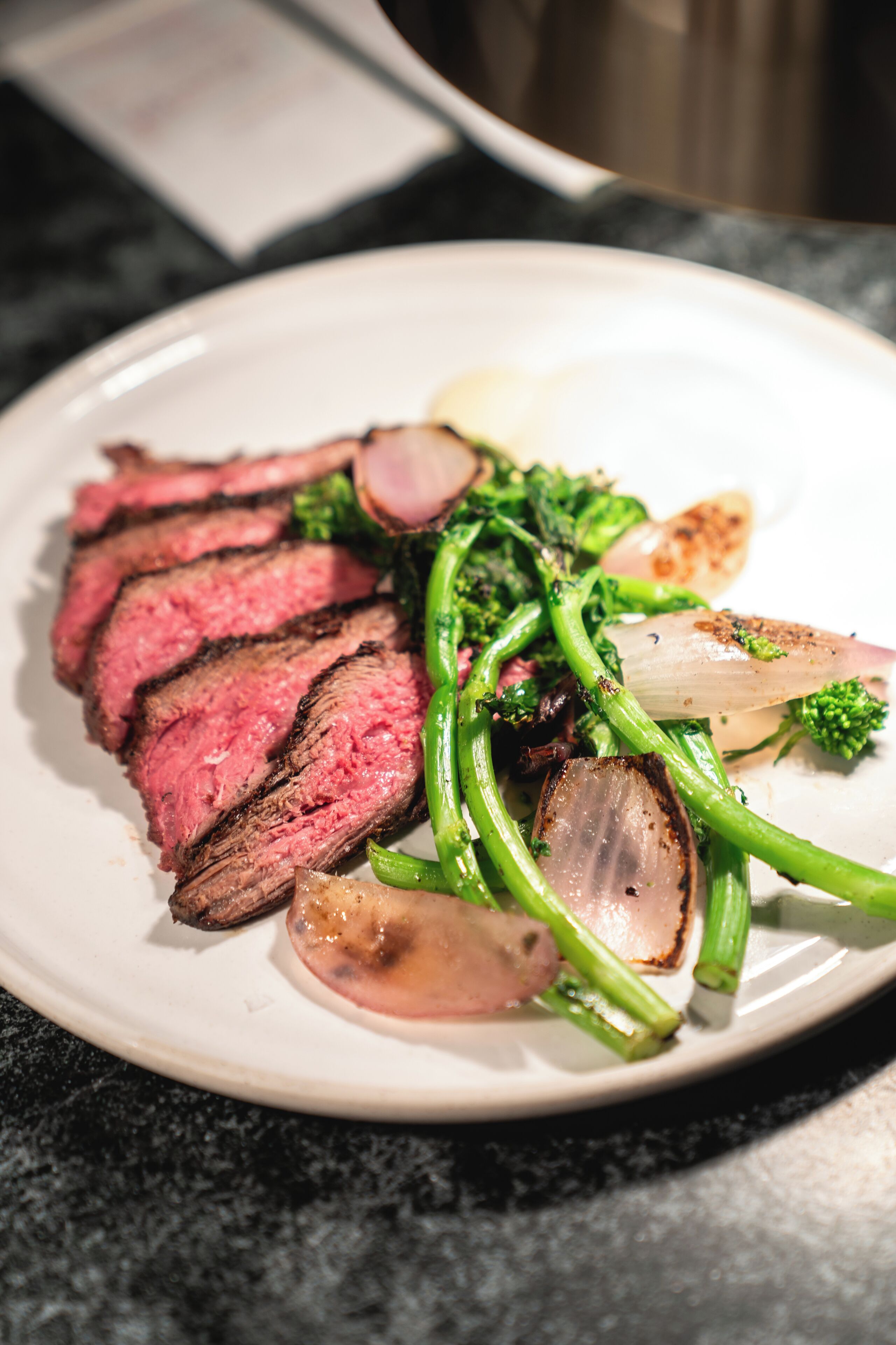 A plate of sliced steak with green vegetables and a slice of onion.