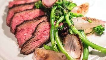 A plate of sliced steak with green vegetables and a slice of onion.