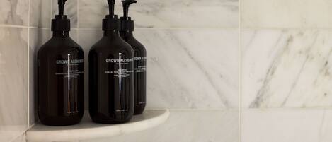 Two bottles of 'Grown Alchemist' shampoo on a white marble shelf in a bathroom.