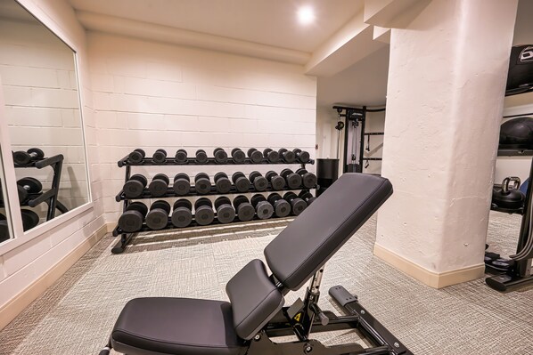 A gym with a bench, a rack of dumbbells, and a mirror.
