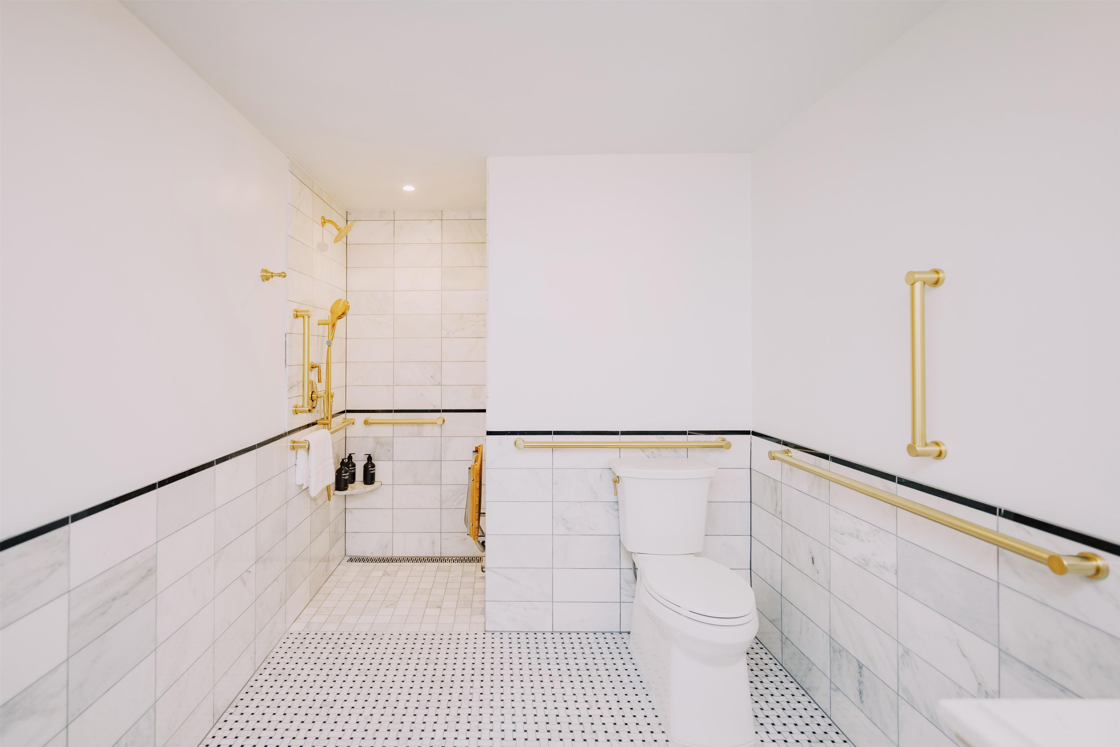 Une salle de bain moderne avec des carreaux blancs, des toilettes blanches et des accessoires dorés.