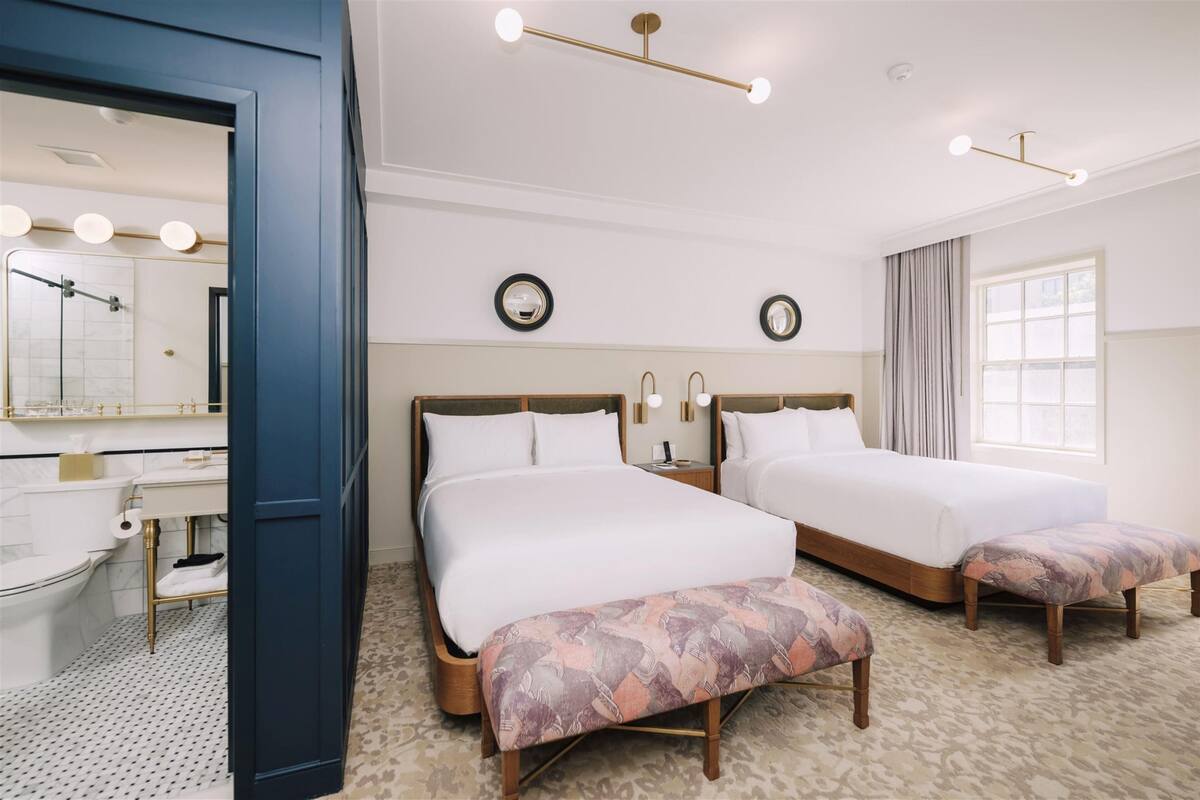 A hotel room with two beds, a bathroom, and a large window.
