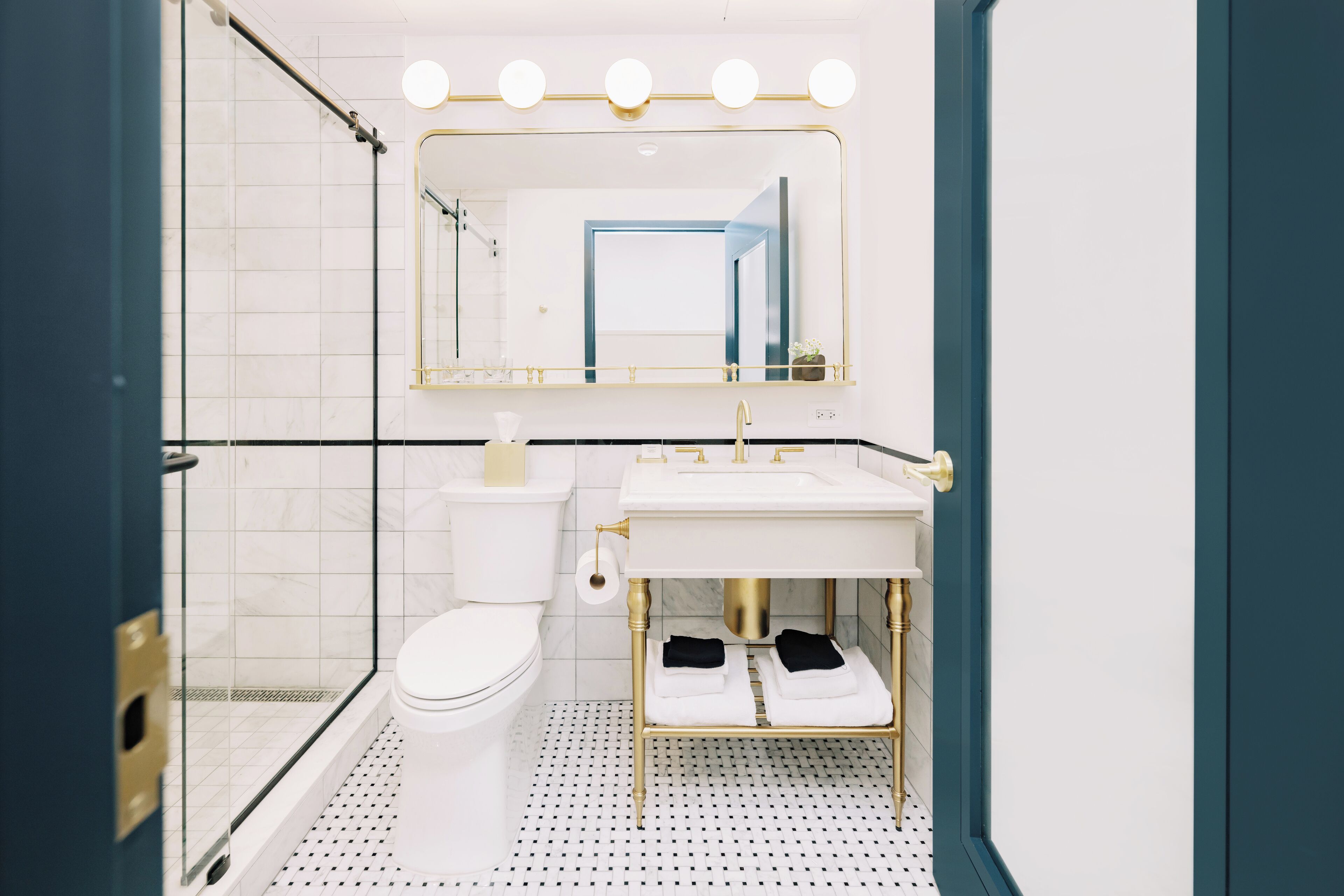 Ein modernes Badezimmer mit Duschkabine aus Glas, einer weißen Toilette, einem goldfarben gerahmten Spiegel und einem weißen Waschbecken mit goldfarbenen Armaturen.
