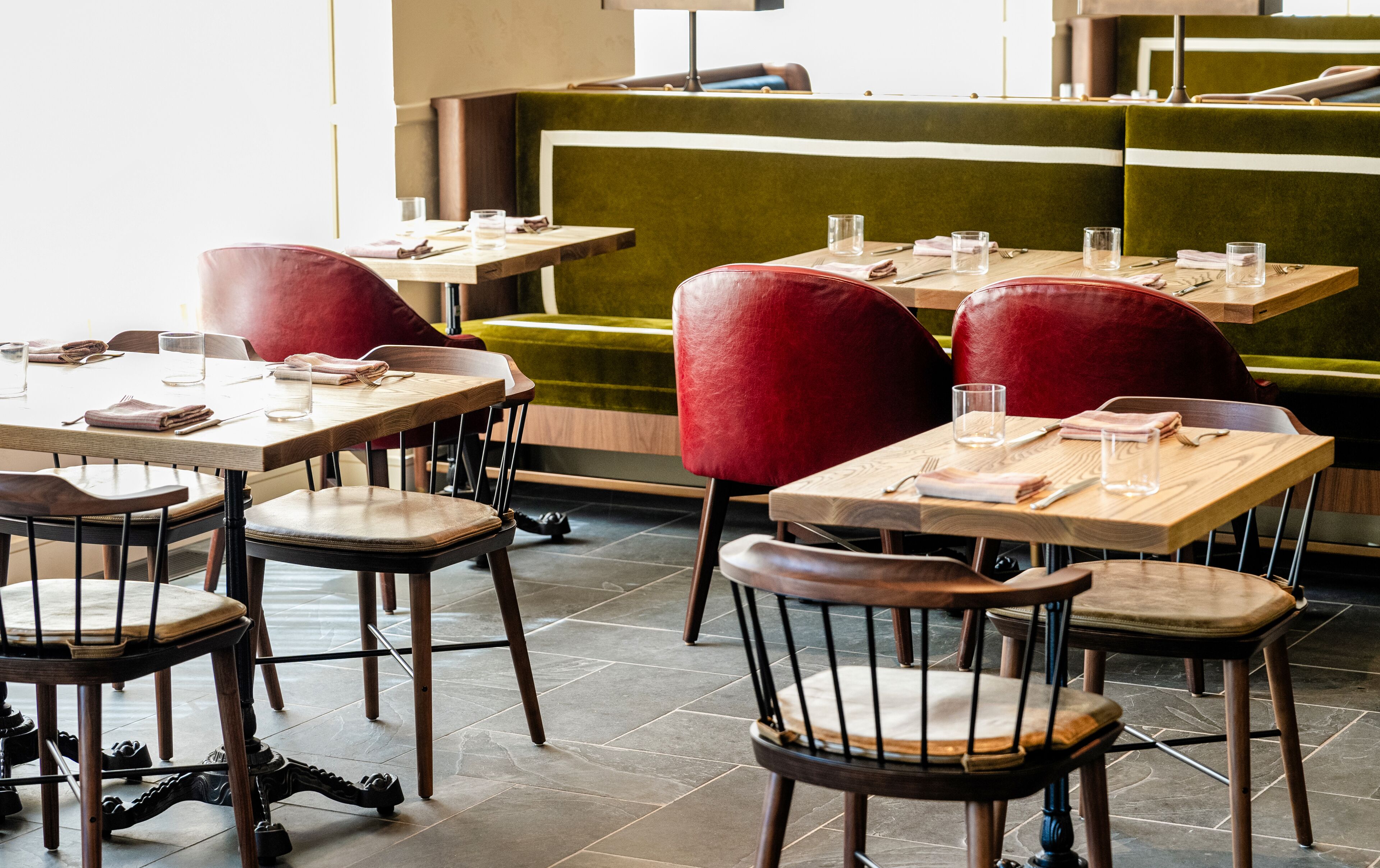 A restaurant interior with wooden tables and red upholstered chairs.