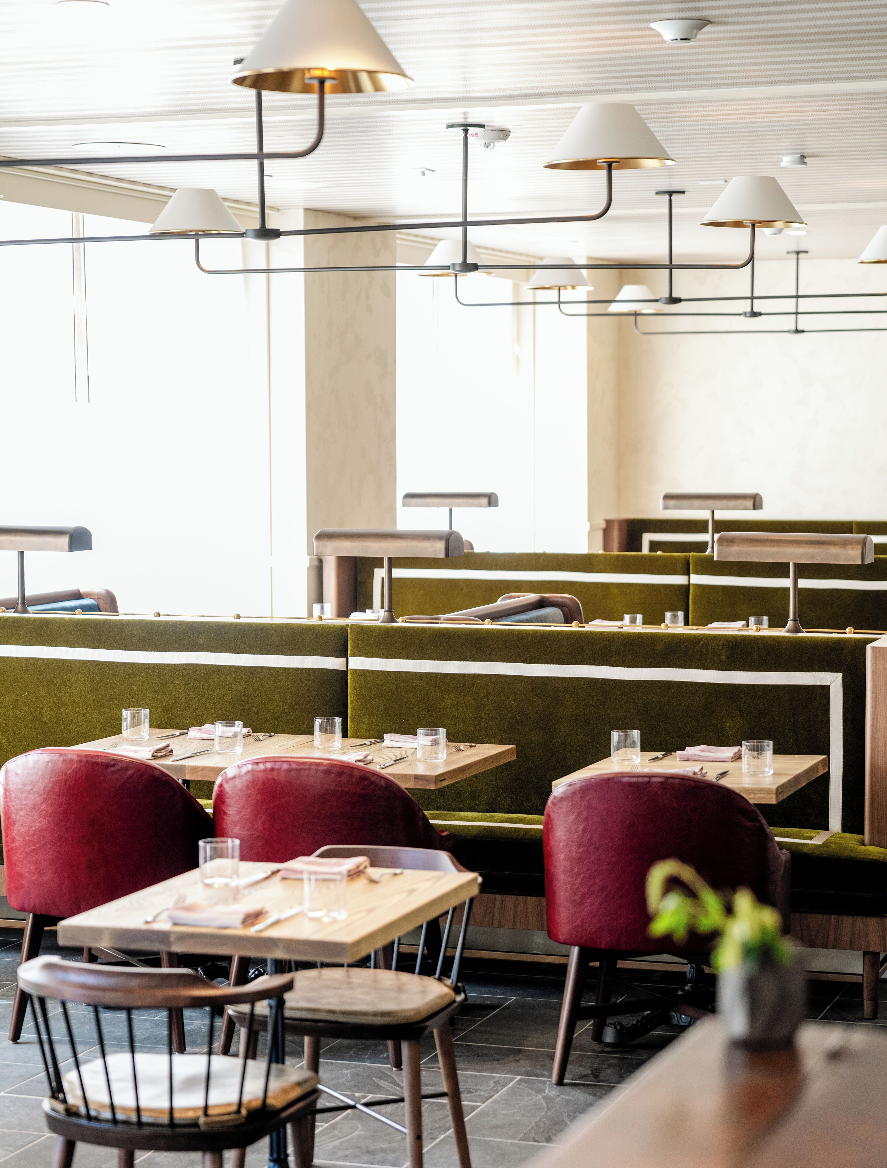 A restaurant interior with green upholstered booths, wooden tables, and metal chairs.