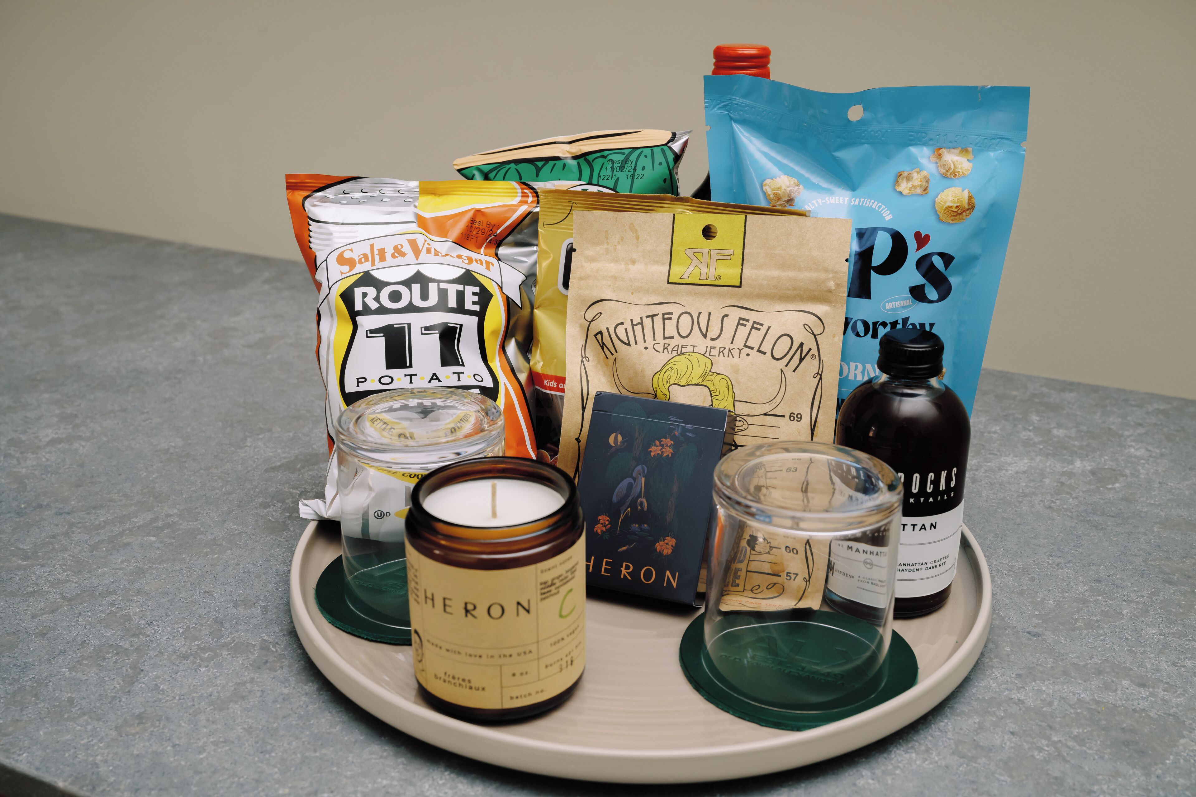 A tray with various food items, including a bag of chips, a jar of peanut butter, a bottle of honey, and a candle.