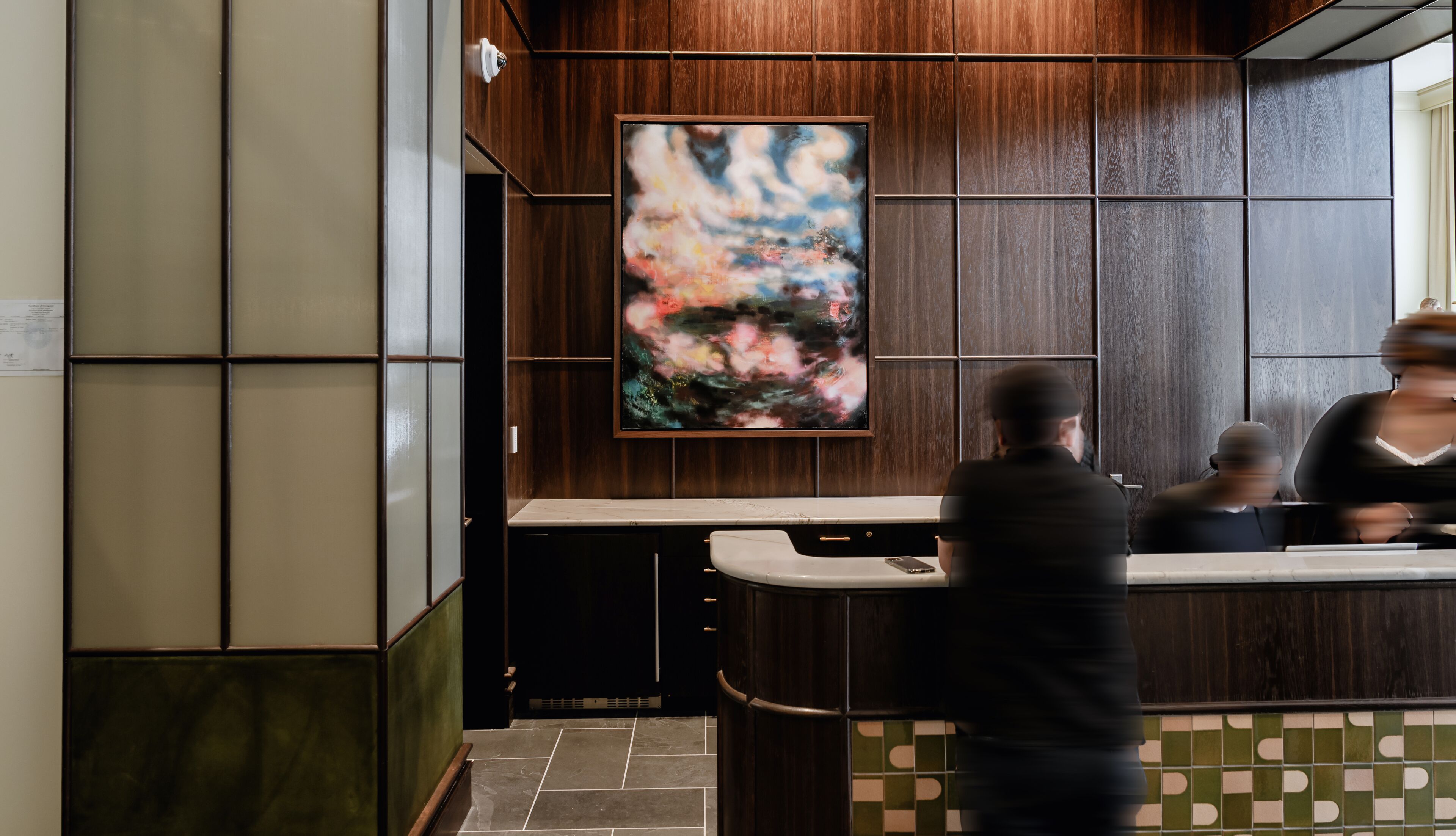 A reception area with a wooden panel wall, a large abstract painting, and a counter with a phone.