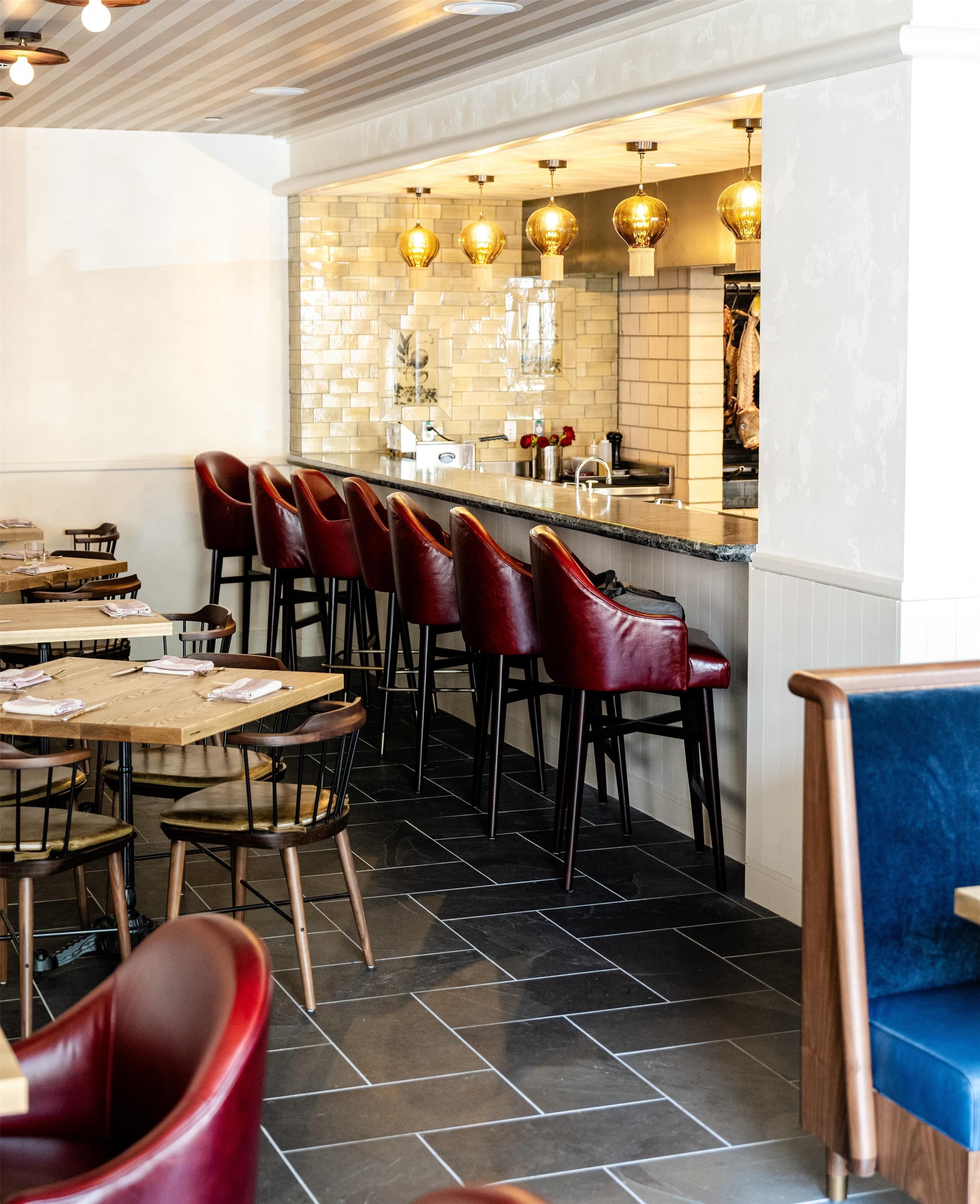Un restaurante con zona de bar, taburetes rojos y piso de baldosas.