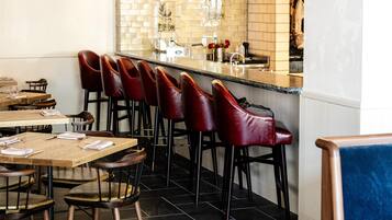 Un restaurante con zona de bar, taburetes rojos y piso de baldosas.