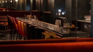 Una zona de bar con una barra alargada, varias sillas y un candelabro peculiar.