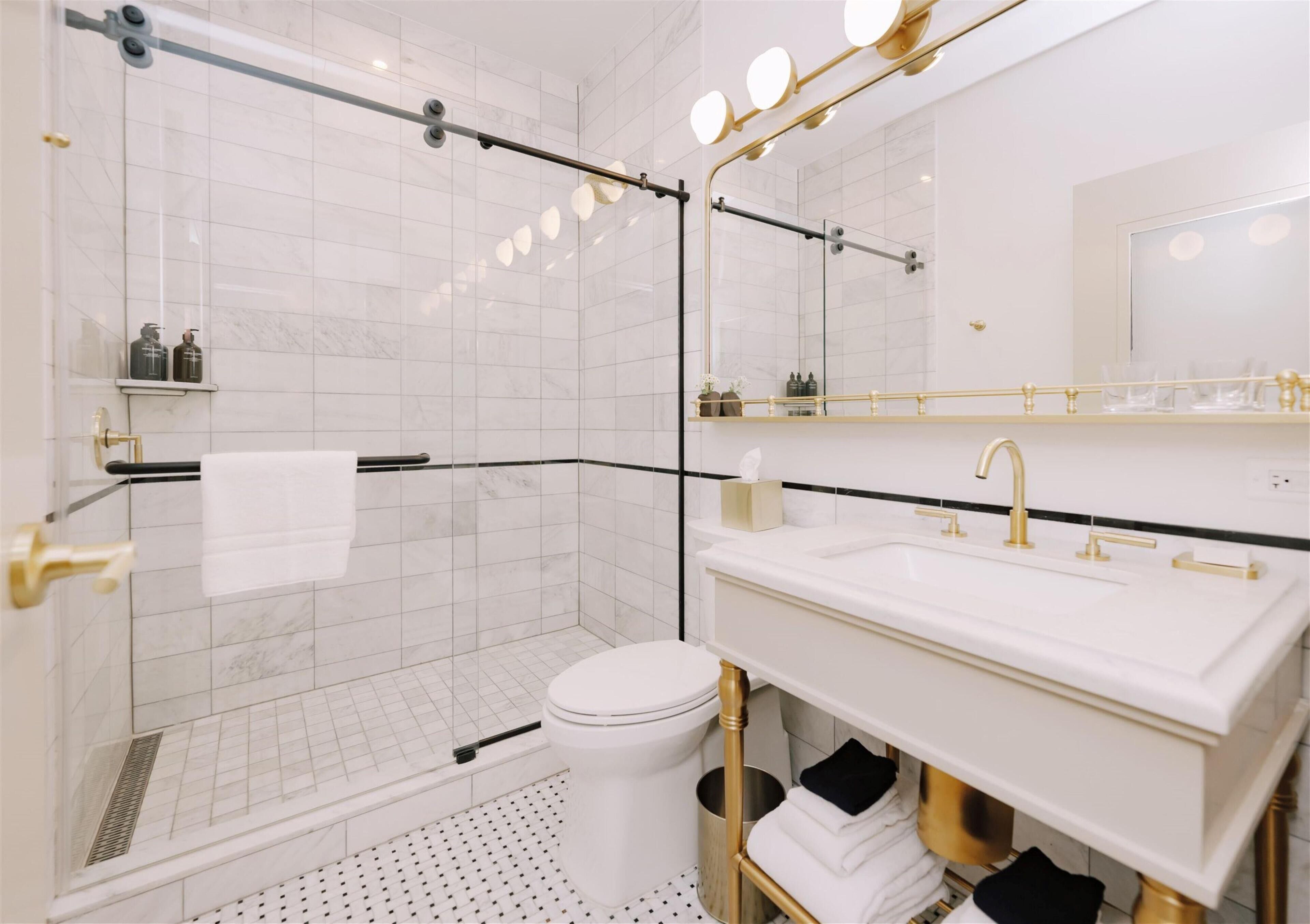 A modern bathroom with a glass shower enclosure, a white toilet, and a vanity with a gold faucet.
